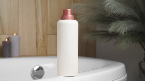 Beige bottle of bubble bath and candles on tub indoors