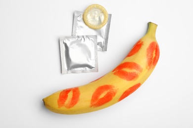 Condoms and banana with lipstick kiss marks on white background, top view. Safe sex