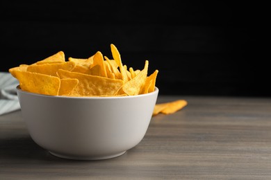 Photo of Tortilla chips (nachos) in bowl on wooden table against dark background. Space for text
