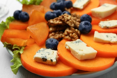 Photo of Delicious persimmon with blue cheese, blueberries and walnuts on plate, closeup