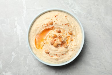 Tasty hummus with garnish in bowl on light grey marble table, top view