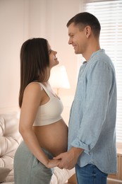 Pregnant young woman with big belly and her husband holding hands together at home