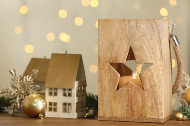 Photo of Wooden Christmas lantern with burning candle and festive decor on table against blurred lights