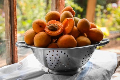 Colander with delicious ripe apricots on table near window