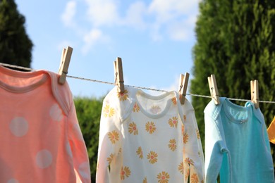 Clean baby onesies hanging on washing line outdoors. Drying clothes