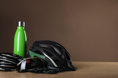 Different cycling accessories on wooden table against brown background, space for text