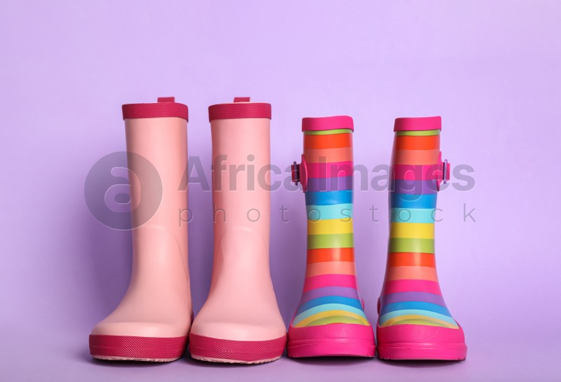Two pairs of rubber boots on violet background