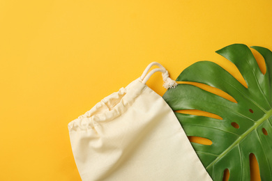 Cotton eco bag and leaf on yellow background, flat lay. Space for text