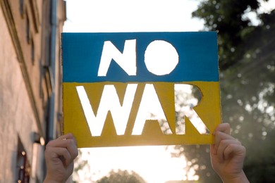 Woman holding poster in colors of Ukrainian flag with words No War outdoors, closeup