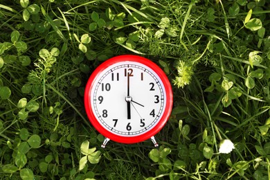 Red alarm clock on green grass outdoors, top view