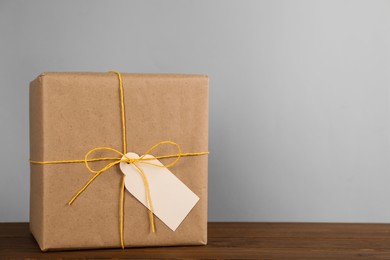 Parcel wrapped in kraft paper with tag on wooden table against light grey background, space for text