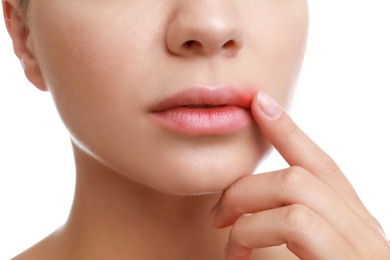 Young woman with cold sore touching lips against white background, closeup
