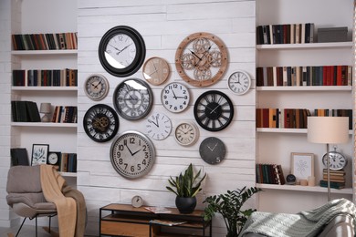 Stylish room interior with console table, comfortable furniture and collection of different clocks on white wall