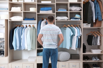 Man choosing outfit from large wardrobe closet with stylish clothes, shoes and home stuff