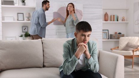 Couple arguing at home, focus on their unhappy teenage boy. Problems in family