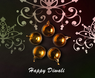 Inscription Happy Diwali and clay lamps on dark background, flat lay 