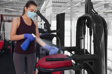 Woman cleaning exercise equipment with disinfectant spray and cloth in gym