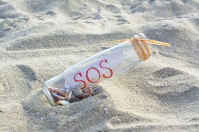 Glass bottle with seashells and message SOS on sand