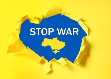 Stop war in Ukraine. Outline map of Ukraine and phrase on blue background, view through torn yellow paper