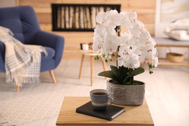 Photo of Beautiful white orchids and cup of tea on wooden table in living room. Interior design