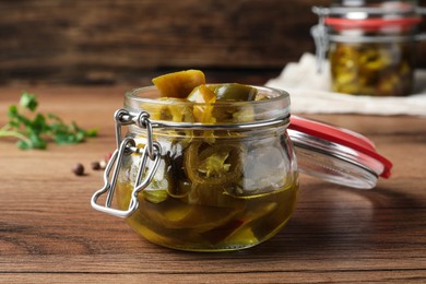 Photo of Glass jar with slices of pickled green jalapeno peppers on wooden table
