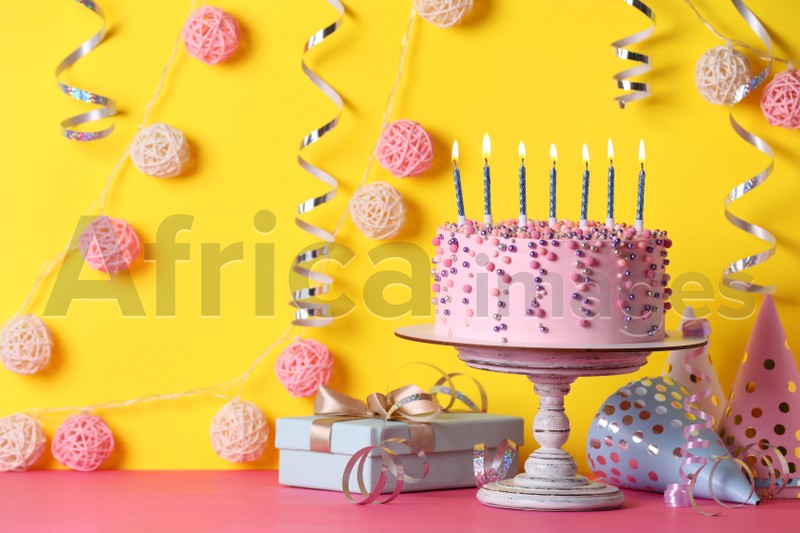 Delicious birthday cake and party decor on pink table against yellow background