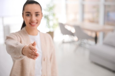 Happy young woman offering handshake indoors, focus on hand. Space for text