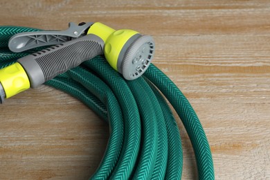 Green rubber watering hose with nozzle on wooden surface, closeup
