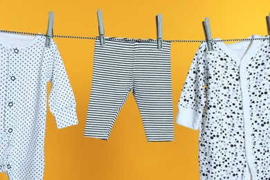 Different baby clothes drying on laundry line against orange background, closeup