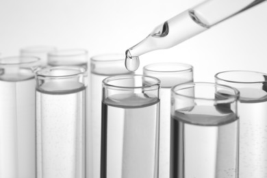 Dripping transparent liquid into test tube on white background, closeup