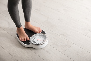 Woman standing on scales indoors, space for text. Overweight problem
