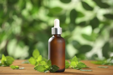 Glass bottle of nettle oil with dropper and leaves on wooden table against blurred background