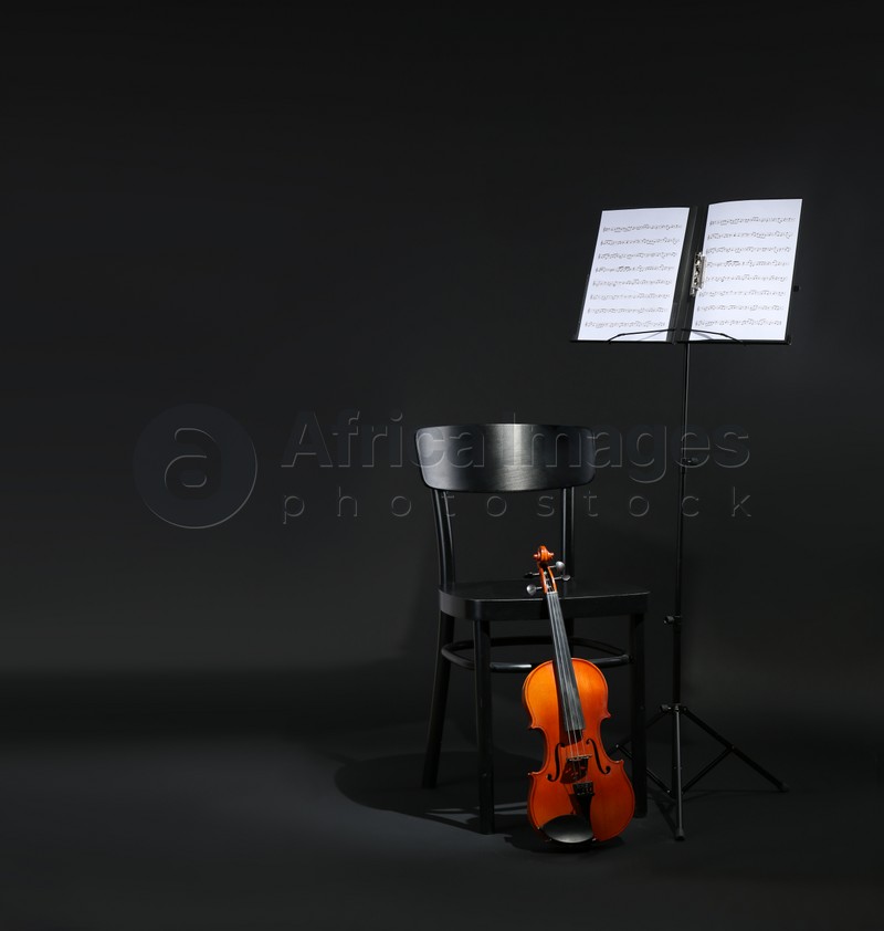 Violin, chair and note stand with music sheets on black background. Space for text