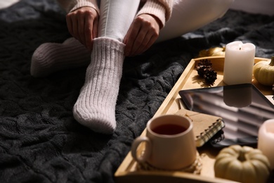 Woman in warm socks relaxing with cup of hot drink on knitted plaid, closeup
