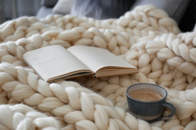 Cup of coffee and book on white knitted plaid indoors