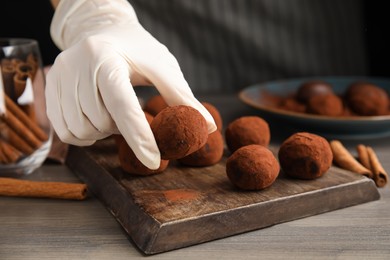 Photo of Confectioner preparing delicious chocolate truffles powdered with cocoa at wooden table, closeup