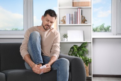 Man suffering from foot pain on sofa at home, space for text