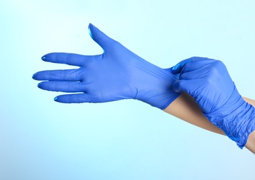 Woman putting on latex gloves against light blue background, closeup of hands
