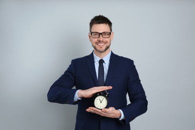Happy businessman holding alarm clock on grey background. Time management