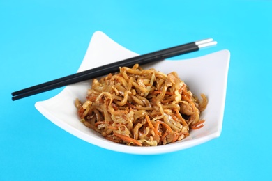 Photo of Plate with Chinese noodles and chopsticks on color background. Food delivery