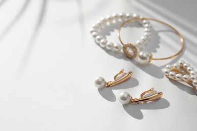 Elegant bracelets, hair clip and earrings with pearls on white table, closeup. Space for text