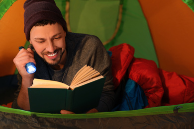 Man with flashlight reading book in tent