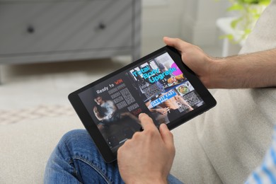 Man reading online magazine on tablet indoors, closeup