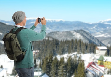 Image of Tourist with travel backpack taking photo in mountains during vacation trip