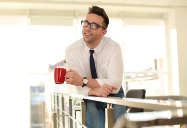 Young businessman with cup of drink relaxing in office during break