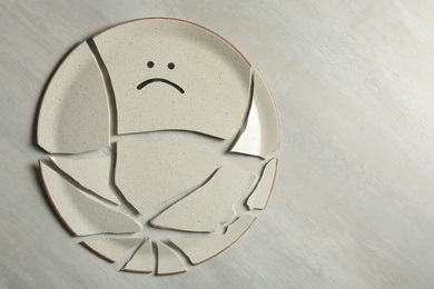 Broken plate with drawn sad face on light background, flat lay. Space for text