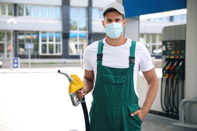 Worker in mask with fuel pump nozzle at modern gas station