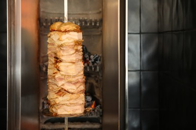 Vertical rotisserie with roasted meat in restaurant kitchen. Space for text