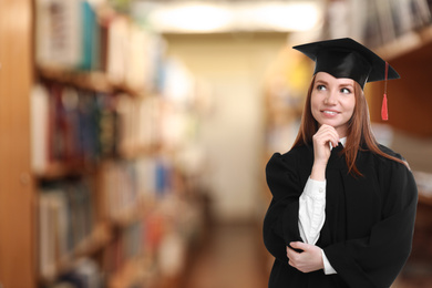 Happy student wearing graduation hat in library, space for text