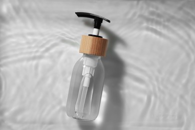 Bottle of cosmetic product in water on white background, top view. Space for text